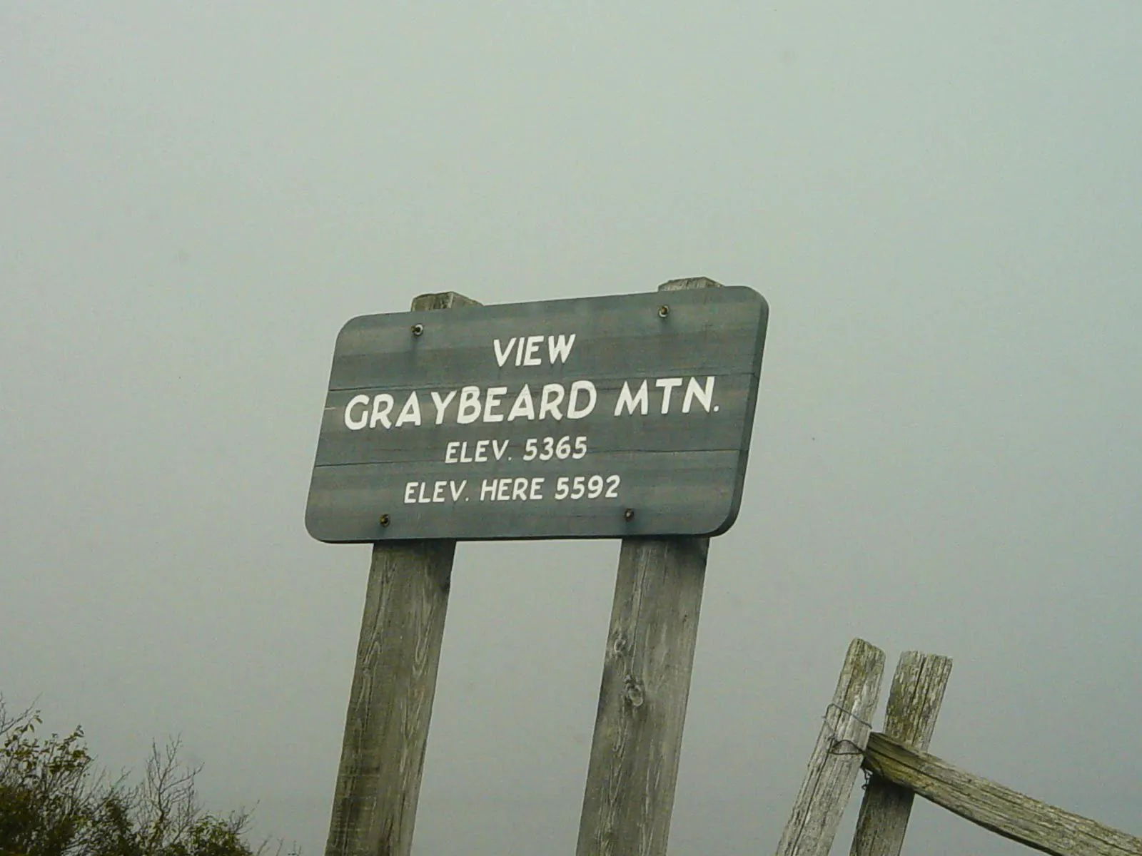 A sign on the blue ridge parkway reading View Graybeard Mountain. The view is completely obscured by fog.