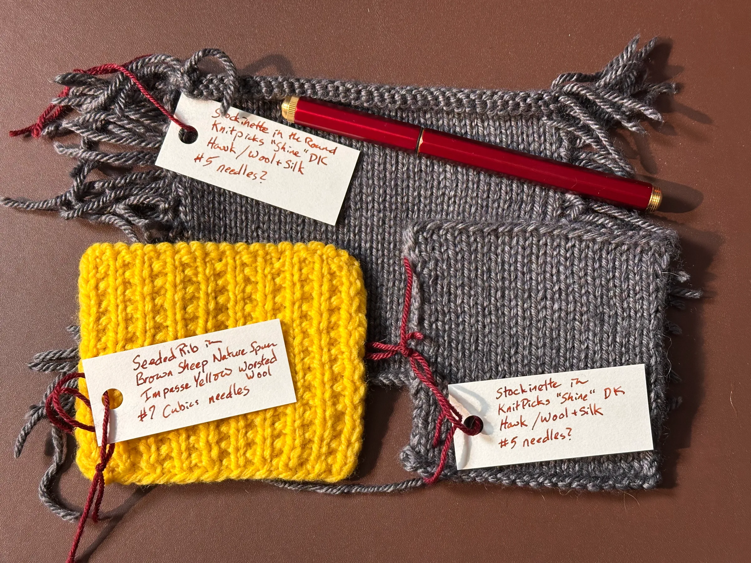 Three knit swatches. The top is a stockinette swatch knit in the round. Bottom left is a yellow swatch in broken rib, and bottom right is a flat-knit stockinette swatch.